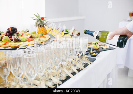 Un bel frutto bar che serve una tavola festiva. Il cameriere versa dello Champagne in bicchieri di vino. Foto Stock