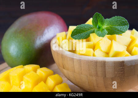La frutta tropicale mango in una piastra su un sfondo di legno, intere o tagliate a fette Foto Stock