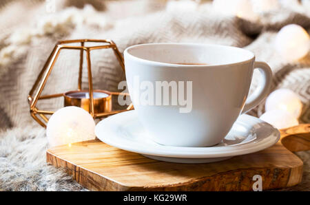 Mattina tazza di caffè a casa, accogliente winter decorazione per interni con coperta e porta candele in background Foto Stock