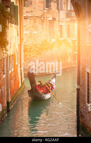 Una gondola con turisti andando giù un piccolo canale foderato con case urbane Foto Stock