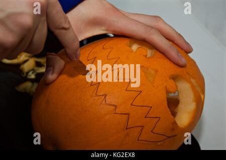 L'uomo carving spooky faccia nella grande zucca in preparazione per la Festa di halloween Foto Stock