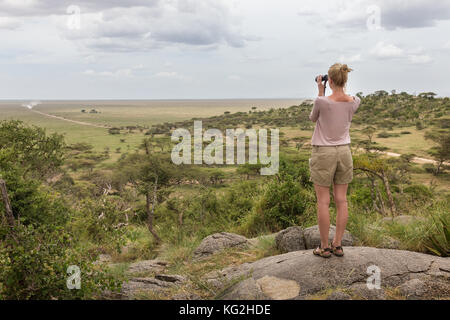 Turista femminile guardando attraverso il binocolo su african safari nel Serengeti National Park. tanzania, afrika. Foto Stock