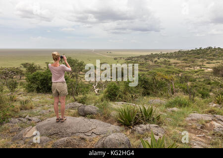 Turista femminile guardando attraverso il binocolo su african safari nel Serengeti National Park. tanzania, afrika. Foto Stock