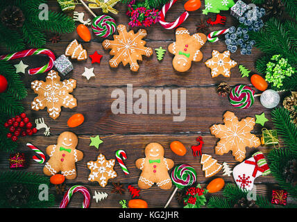 Il natale di panpepato biscotti fatti in casa su un tavolo di legno con canditi, albero di natale rami e Nuovo Anno decorazioni. xmas sfondo del telaio Foto Stock