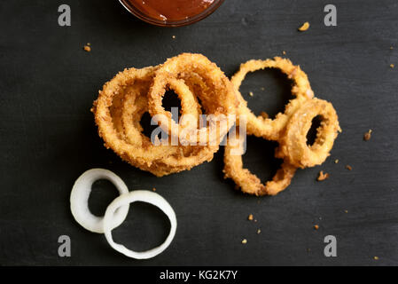 Croccanti anelli di cipolla fritti su sfondo scuro, vista dall'alto Foto Stock