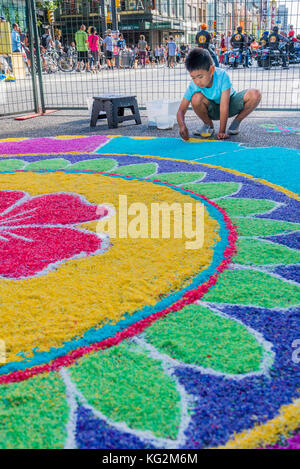 Ragazzo aggiunta di riso alla grande mandala Rangoli piano decorazione India Live Street Festival celebrazione, Vancouver, British Columbia, Foto Stock