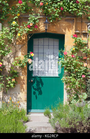 Porte verdi in un inglese cottage in pietra calcarea circondata dalla fioritura di rose rampicanti, lavanda Foto Stock