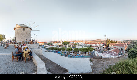 Vista panoramica ad alta risoluzione dei mulini a vento, dove la gente mangia e beve in un bar vicino in una giornata di sole nella città di Alacati, una destinazione popolare per i viaggi Foto Stock