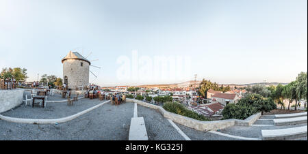Vista panoramica ad alta risoluzione dei mulini a vento, dove la gente mangia e beve in un bar vicino in una giornata di sole nella città di Alacati, una destinazione popolare per i viaggi Foto Stock