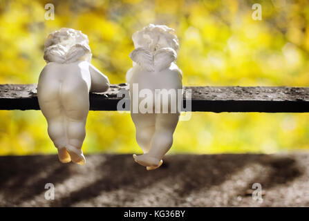 Funny white angeli di ceramica con piccole ali sono vista posteriore in autunno park. Foto Stock