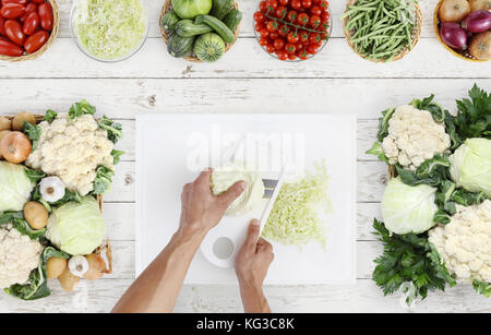 Le mani per la cottura di taglio sopra il cavolo bianco sul tagliere con verdure fresche su cucina bianco piano di lavoro in legno, copia spazio, vista dall'alto Foto Stock