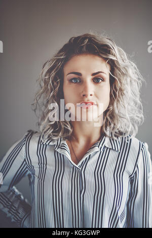 Ritratto di un concentrato giovane imprenditrice con la bionda in piedi da solo in un ufficio con la sua mano sulla hip Foto Stock