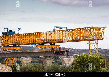 Autostrada autostrada o costruzione di ponti con grandi gantry gru di sollevamento in tratti di strada tra pilastri. Sicilia, Italia Foto Stock