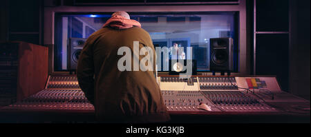 Ingegnere del suono lavora al pannello di controllo audio con il cantante a cantare in sala di registrazione in background. I musicisti che producono musica in registrazioni professionali Foto Stock