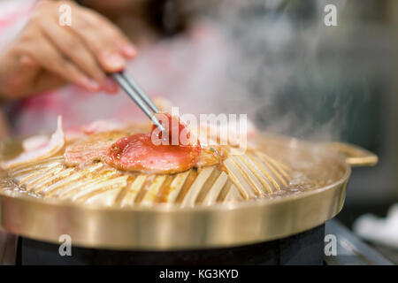 Mano azienda chopstick con grigliate di carne di maiale coreano yakiniku alla griglia in stile giapponese. Foto Stock