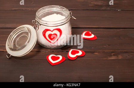 Vaso con neve e un cuore in lui. uno sfondo dal colore marrone, schede su schede molti cuori sono sparse, il vasetto di vetro, un cuore da tessuto si trova in Foto Stock
