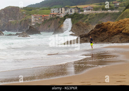 Bakio, Spagna - luglio 4, 2016: sconosciuto turisti su una spiaggia. Il giovane uomo costi sulla spiaggia e osserva una tempesta Foto Stock