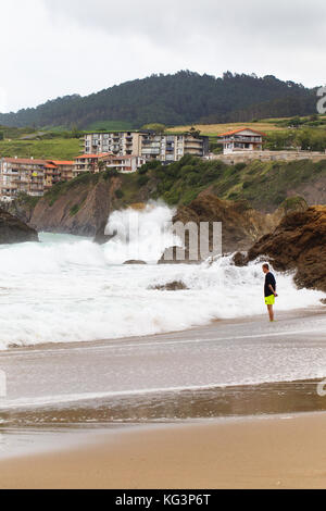 Bakio, Spagna - luglio 4, 2016: sconosciuto turisti su una spiaggia. Il giovane uomo costi sulla spiaggia e osserva una tempesta Foto Stock