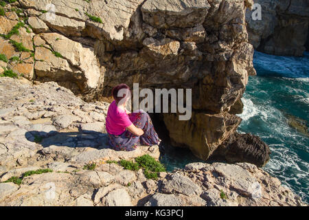 Spagna Cantabria - luglio 3, 2016: la donna sconosciuta sulla costa dell'oceano. la donna siede sulla costa alta e guarda lontano, una vista dal retro. sunny summ Foto Stock