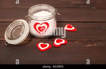 Vaso con neve e un cuore in lui. uno sfondo dal colore marrone, schede su schede molti cuori sono sparse, il vasetto di vetro, un cuore da tessuto si trova in Foto Stock