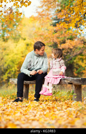 Felice fratello e sorella sono seduto sulla panchina a parlare e ridere. In natura, camminare all'aria aperta Foto Stock