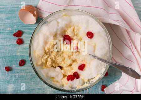 Impasto per cottage cheese casseruola, shell e asciugamano, vista dall'alto. mantecato bianchi e bacche rosse di formaggio in una ciotola di vetro con un cucchiaio, un blu w Foto Stock