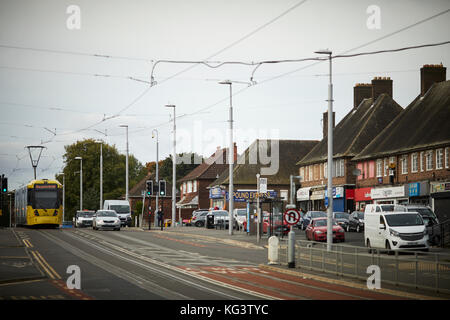 Un giallo Metrolink di Manchester a tram Hollyhedge Road, Benchill, Wythenshawe. Il passaggio di un corteo di indipendenti negozi locali Foto Stock