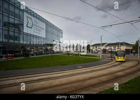 Un giallo Metrolink di Manchester a tram Hollyhedge Road, Benchill, Wythenshawe. passando il Manchester College moderno edificio si è degnato Foto Stock