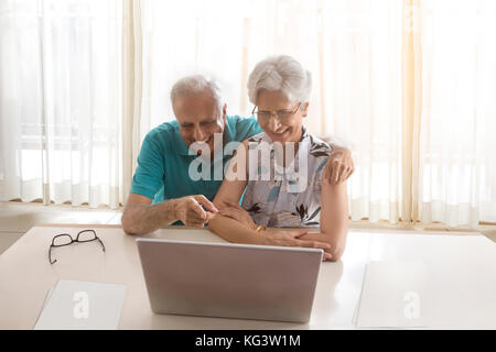 Coppia senior utilizzando laptop seduta a tavola Foto Stock