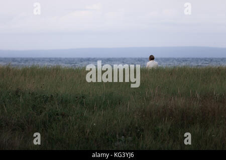 Antigonish County, Canada - 28 agosto 2017: una donna si siede e si gode della vista lungo Nova Scotia del nord della costa al tramonto. Foto Stock