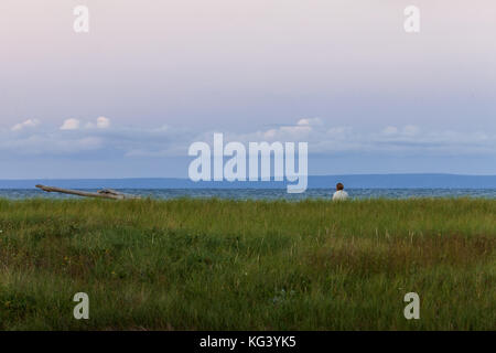 Antigonish County, Canada - 28 agosto 2017: una donna si siede e si gode della vista lungo Nova Scotia del nord della costa al tramonto. Foto Stock