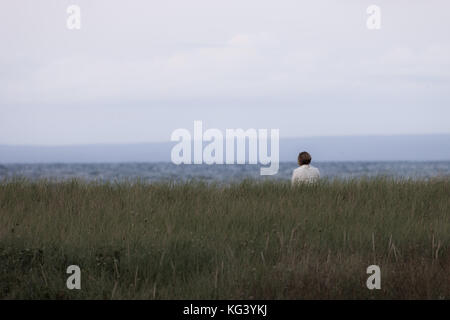 Antigonish County, Canada - 28 agosto 2017: una donna si siede e si gode della vista lungo Nova Scotia del nord della costa al tramonto. Foto Stock