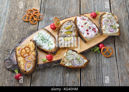 Abbondante spuntino con diversi tipi di si diffonde su pane contadino servita su un vecchio tavolo in legno Foto Stock
