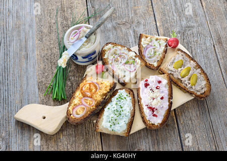 Abbondante spuntino con diversi tipi di si diffonde su pane contadino servita su un vecchio tavolo in legno Foto Stock