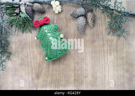 Addobbi natale realizzati in crochet, sul legno rustico sfondo inquadrato con foglie di vischio, abete e pino cono. top visualizzare e copiare lo spazio. Foto Stock