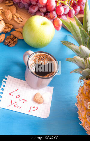 Frutta fresca e i dadi su un blu tavolo in legno, una tazza di caffè arabo e un foglietto di carta con amore il tuo messaggio a forma di cuore lo zucchero su di esso. Foto Stock