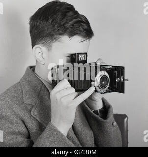 Degli anni Cinquanta, la fotografia storica, immagine mostra un giovane ragazzo di guardare attraverso il mirino su un formato del supporto di piegatura Kodak fotocamera a pellicola, con Anaston obiettivo F6.3, Inghilterra, Regno Unito. Foto Stock