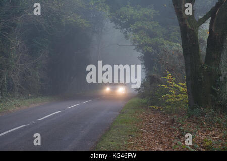 Un'auto con fari accesi durante la guida lungo una strada di campagna in nebbia fitta Foto Stock