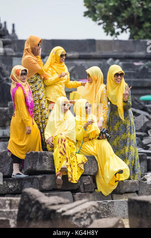 Donne che indossano hijab e giallo abiti tradizionali sedersi sulle rovine del tempio di Prambanan Foto Stock