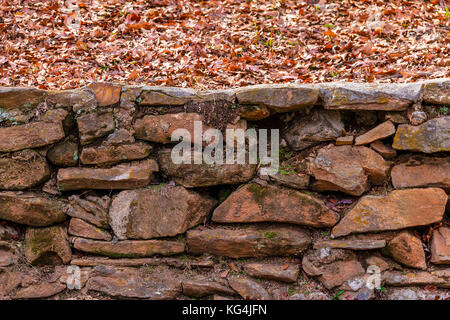 La pietra grezza parete e foglie secche in autunno park Foto Stock