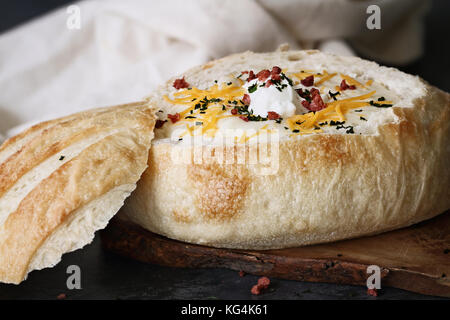 Calda zuppa di patate in un pane di pasta acida ciotola con panna acida, il formaggio cheddar, essiccato di erba cipollina e il bacon a pezzetti. estrema profondità di campo con il selettivo Foto Stock