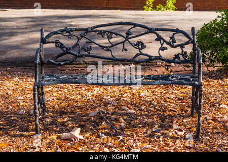 Il ferro battuto banco ornamentali closeup e foglie secche sotto il cimitero di Oakland nella soleggiata giornata autunnale, Atlanta, Stati Uniti d'America Foto Stock