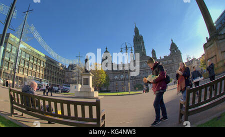 La gente del posto e turisti di mangiare fast food pesce e patatine godere seduti al sole sulle panchine di George Square in una prospettiva di fish eye lens shot Foto Stock