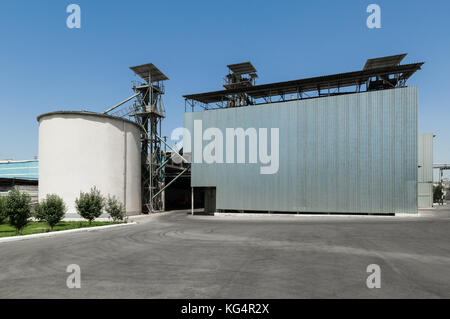 Serbatoio di stoccaggio e un edificio su un'azienda sotto un cielo blu. Impianti industriali pesanti Foto Stock