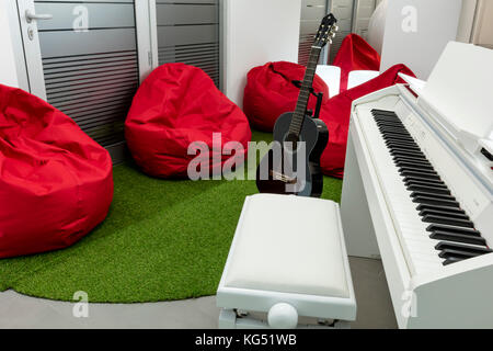 Musica moderna-camera, con pianoforte bianco e nero chitarra; rosso beanbags in background. Foto Stock