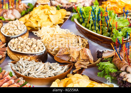 Tabella per banchetti con prodotti a base di carne, pistacchi, olive, pesci secchi, patatine e altri snack nel ristorante Foto Stock