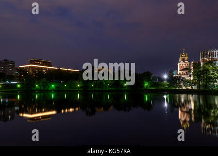 Pittoresca vista notturna di Mosca con il monastero di Novodevichy, pareti di pietra bianca, verde di alberi, luci e belle riflessioni di loro in acqua Foto Stock