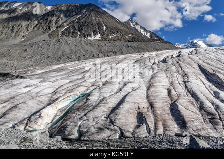 Bellissima vista dal basso sulle montagne e sul ghiacciaio con neve e con crepe e rompe il ghiaccio contro lo sfondo del cielo blu e nuvole in estate Foto Stock