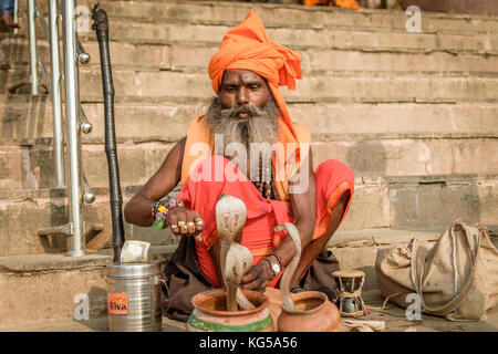 Un indiano non identificato serpente incantatore in turbante giocando sulle mani prima di Snake in un cesto a varanasi ghat. Foto Stock