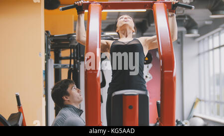 Fitness-club - giovane donna esegue il pull-up con pullman maschio Foto Stock